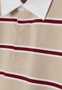 Polo beige avec col blanc, rayures horizontales rouges et blanches, et un petit logo brodé sur la poitrine.