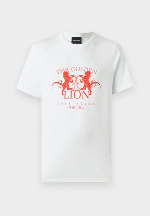 Hvit bomulls t-skjorte med en rød grafisk trykk av to løver og teksten "THE GOLDEN LION FREE HOUSE" i en sirkulær design. Korte ermer.