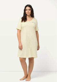 Keltainen yöasu pehmeästä kankaasta, jossa on lyhyet hihat, napitettu V-pääntie ja monivärinen brodeeraus yksityiskohtana rinnassa.