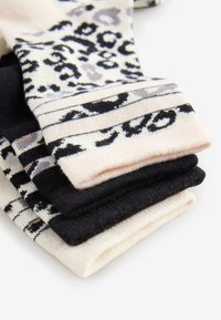 Stapel gefalteter schwarzer, weißer und beiger Socken, einige mit Leoparden- und Streifenmustern, auf weißem Hintergrund dargestellt.