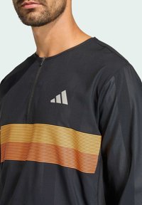 Black long-sleeve shirt featuring a quarter-zip neckline. It has an orange to yellow horizontal striped pattern across the chest and a logo.
