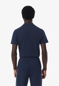 Mörkblå polo-tröja med krage och korta ärmar, visad från baksidan. Matt textur, inga synliga mönster eller logotyper.