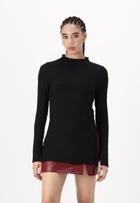 Black long-sleeve top with a ribbed texture and ruffled neckline, paired with a short burgundy leather skirt featuring a side slit.