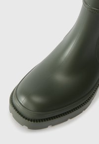 Groene rubberlaars met een ronde neus, een gestructureerde zool en subtiele verticale lijnen op de schacht. Gladde afwerking met een stevige constructie.