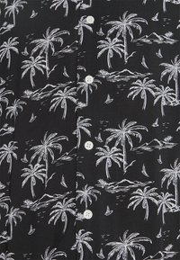 Musta lyhythihainen paita, jossa on valkoinen kuvio, jossa on palmuja, vuoria ja purjeveneitä, sekä valkoiset napit kauluksessa.