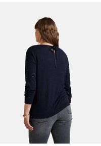 Maglione a maglia blu navy con maniche lunghe, dotato di scollatura rotonda e dettaglio con fiocco sul retro. Sottile motivo a stelle sulle maniche. Texture liscia.