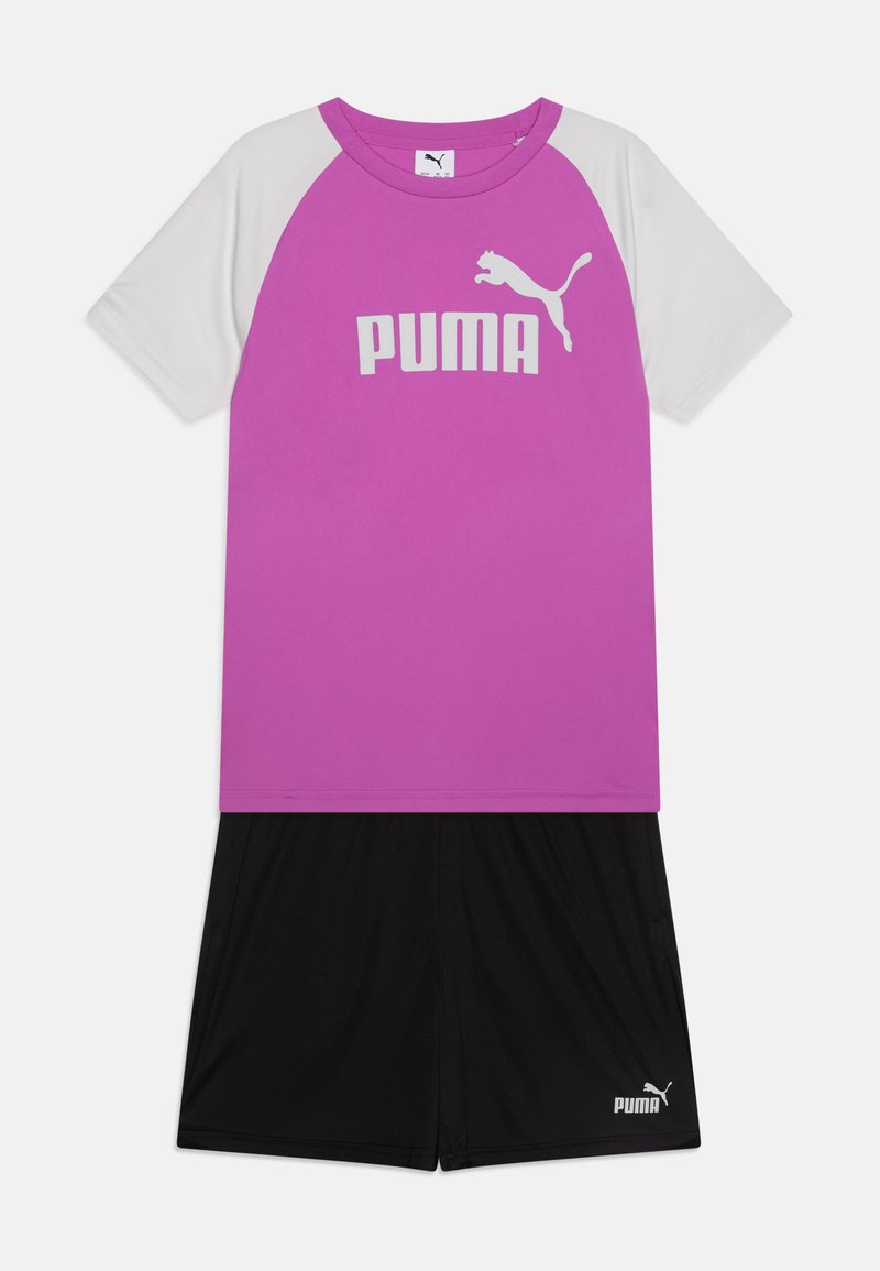 Fialové a biele tričko s krátkym rukávom s logom "PUMA", v kombinácii s čiernymi šortkami s malým logom "PUMA" na nohe.