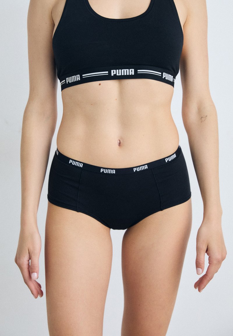Set di reggiseno sportivo e mutande nere realizzato in tessuto morbido, caratterizzato da un band con logo e accenti bianchi. Il design include una forma aderente.