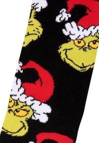 Calzini neri con volti del Grinch verdi e occhi gialli, che indossano cappelli di Babbo Natale rossi, con accenti di pelliccia bianca. Texture morbida in maglia.