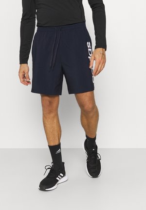 Shorts de sport bleu marine avec une taille à cordon et un logo blanc. Portés avec des chaussures noires et des chaussettes à rayures blanches.