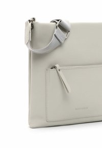 Borsa in pelle grigia chiara con superficie texture, tasca frontale con zip e tracolla in tessuto attaccata con hardware metallici.