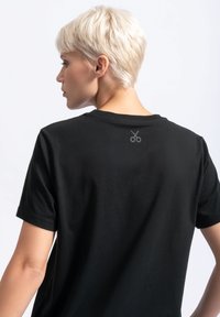 Zwarte katoenen t-shirt, korte mouwen, ronde hals, met een kleine schaarafbeelding op de bovenrug, zachte textuur, casual pasvorm.