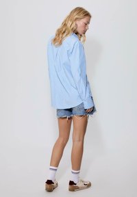 Chemise oversize rayée bleu et blanc, shorts en denim et baskets. La chemise possède un col et des manches longues.