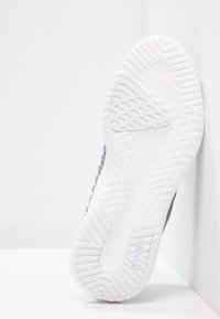 Grå idrottssko med en texturerad ovandel och en vit gummisula med ett zigzag-mönster. Sidologotyp synlig i vitt.