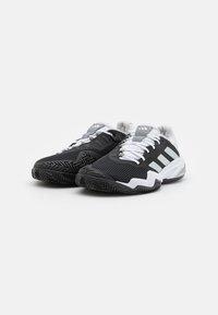 Baskets de sport en mesh noir avec des accents blancs, dotées d'une semelle texturée et de lacets. Trois rayures blanches sur le côté, conçues pour le sport.