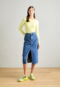 Långärmad ribbad topp i ljusgul färg kombinerad med en högmidjad jeanskjol med slits fram. Skorna består av klara gula sneakers.