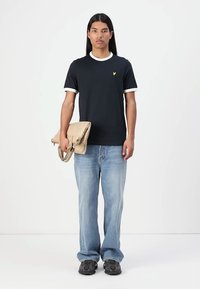 T-shirt marine avec des bordures blanches, jeans bleu clair et baskets noires. Tient un sac beige. Design simple et décontracté.