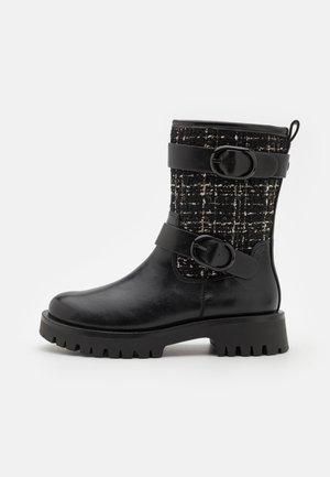 Bota de tobillo de cuero negro con parte superior de tweed, que cuenta con dos correas con hebilla, una suela resistente y un acabado texturizado.