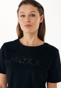 Černé bavlněné tričko s kulatým výstřihem a krátkými rukávy, ozdobené flitrovým logem "MEXX" na přední straně.