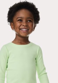 Camisa de manga larga de color verde claro con textura, usada por un niño, que presenta un cuello redondeado y una tela suave.