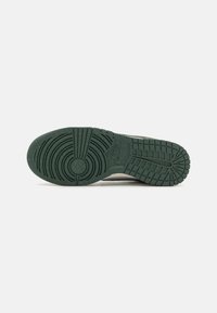 Nike apavu zole ar dziļi zaļu gumijas pamatni, kurai ir teksturētas rakstu formas, tostarp aplīši un rievas, lai nodrošinātu saķeri, kā arī logotipa nospiedums.