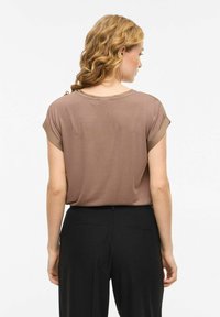 Haut marron à manches courtes retroussées, fabriqué en tissu doux. Associé à un pantalon noir avec deux poches arrière.