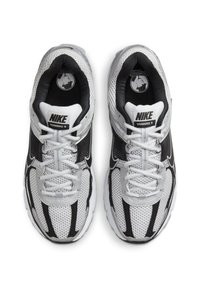 Nike Vomero 5 superge, ki imajo mrežasto zgornji del v beli in črni barvi, udobno podplat in izstopajoč sistem vezalk za podporo.