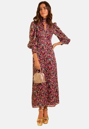 Abito maxi con un motivo ikat colorato, maniche puff lunghe, collo alto e dettagli plissettati. Abbinato a una borsa morbida rosa e tacchi a piattaforma dorati.