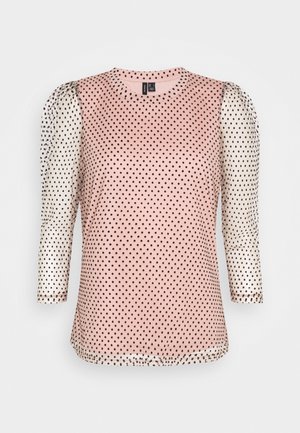 Haut rose avec des pois noirs, présentant des manches blanches semi-transparentes avec des pois noirs, un col rond et des manches trois-quarts.