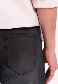 Jean foncé en denim, avec une poche arrière dotée d'un contour brodé, vue en gros plan avec une chemise rose clair visible au-dessus.