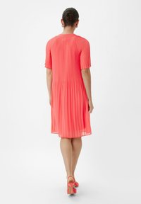 Krótka różowa sukienka z plisami, krótkimi rękawami i okrągłym dekoltem. Gładka tekstura, lekko opływający fason, kończy się powyżej kolan.