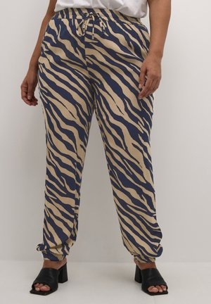 Pantalons amples en tissu beige avec des rayures zèbres bleu marine, dotés d'une taille élastique avec cordon de serrage et de poignets fuselés.