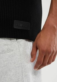 Czarny sweter prążkowany z teksturowanym wykończeniem, z matowym czarnym metkiem z logo. Jasnoszare spodnie dresowe z delikatnym wypukłym detalem logo.