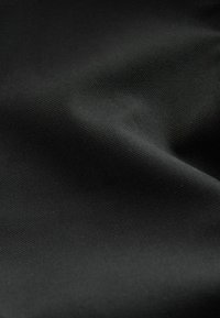 Črna tkanina z gladko teksturo in subtilnim vzorcem tkanja; svetloba in senca ustvarjata nežne gube po površini.