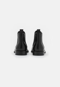 Botas de cuero negro hasta el tobillo con un acabado suave, punteras redondeadas y tacones planos. La parte trasera cuenta con tiradores para facilitar su uso.