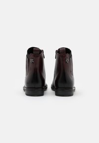 Bottines en cuir de couleur bourgogne foncé, avec des fermetures à glissière sur le côté, des panneaux élastiques et un accent métallique décoratif sur le talon.