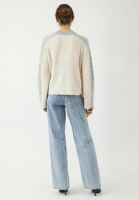 Un pull crème et gris avec un col rond et des manches raglan, associé à un jean large bleu clair et des chaussures à talons noires.