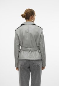 Grå skinnjakke med belte i midjen, bred krage og skulderlapper. Bakperspektiv viser en glatt tekstur og skreddersydd passform.