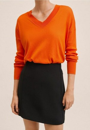 Orange V-Ausschnitt-Pullover aus weichem Strickstoff, kombiniert mit einem taillierten schwarzen Minirock. Das Outfit hat lange Ärmel und eine glatte Textur.
