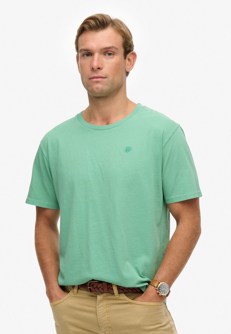 Lichtgroen katoenen t-shirt met een ronde hals en korte mouwen, voorzien van een subtiel logo op de borst, gecombineerd met kaki broek en een bruine riem.