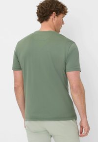 T-shirt verde oliva a maniche corte in tessuto morbido, con collo a giro standard e texture liscia, senza pattern o decorazioni visibili.