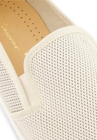 Chaussure à enfiler couleur crème avec une tige en maille texturée arborant un motif tissé et des bordures lisses et renforcées. Semelle intérieure douce et rembourrée visible.