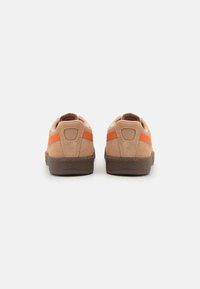 Sneaker in suede marrone con accenti arancioni, suola piatta in gomma, tacco arrotondato e collo imbottito. Design bicolore con superfici lisce e testurizzate.