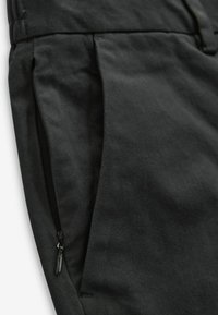 Schwarze Hose mit glatter Textur, ausgestattet mit einer seitlichen Reißverschlusstasche, klaren Falten und einem strukturierten Bund für eine schlanke Silhouette.