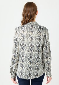 Bluzka z długim rękawem w wzór węża, z jasnobeżowym tłem i ciemnoszarymi wzorami, z zapinanymi mankietami i klasycznym kołnierzykiem.