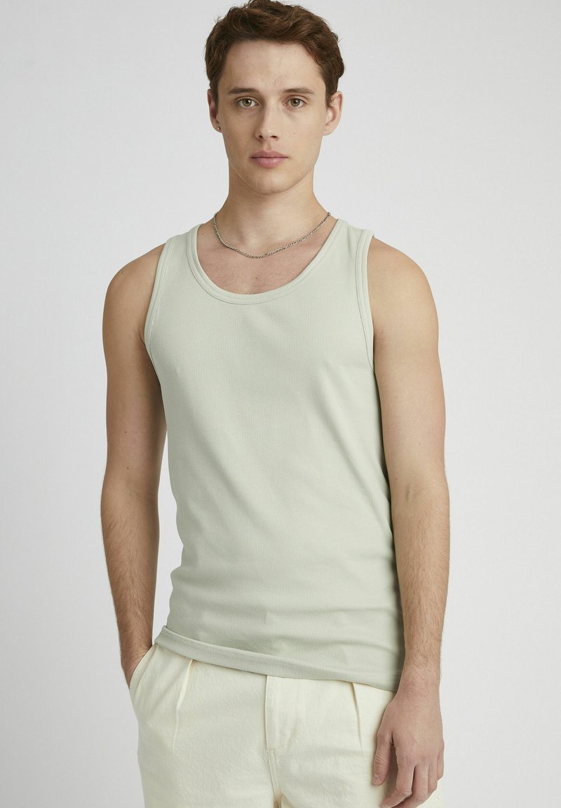 Débardeur côtelé vert clair avec un col rond. Le tissu est doux, ajusté et sans motifs. Porté avec un pantalon couleur crème.