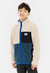 Fleece jacket in cream, teal, and black with a blue zipper. Features a chest pocket and textured fabric, providing warmth and comfort.