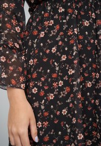 Svart blomsterkjole med et gjennomsiktig, lett stoff og et delikat mønster av røde og hvite blomster, myk tekstur og puffete ermer.