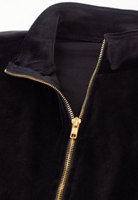 Must sametist jakk kuldse metallist lukuga, mis on osaliselt lahti, näidates krae all musta sisevoodrit.