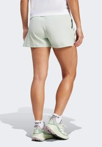 Pantalones cortos deportivos de color verde claro con un diseño acampanado, textura suave y bolsillos laterales, combinados con zapatillas grises y verdes y calcetines blancos.